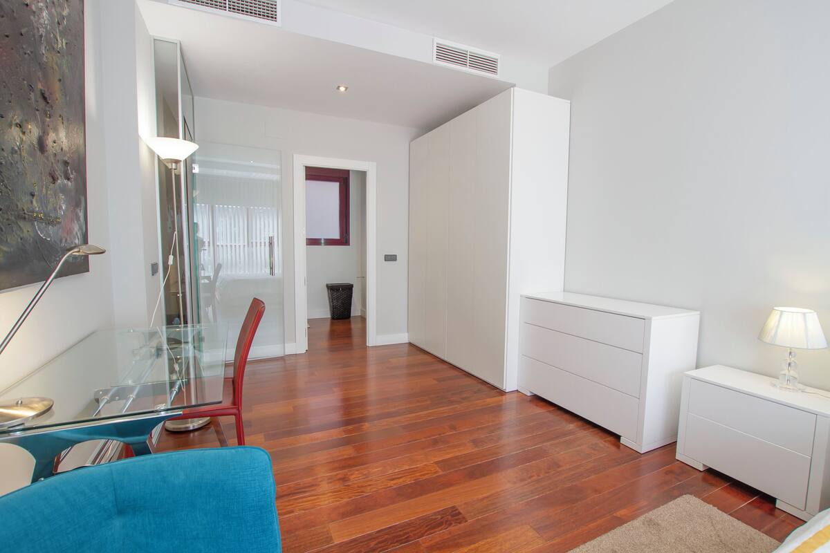A modern living room with a glass dining table, a blue sofa, and a white cabinet.