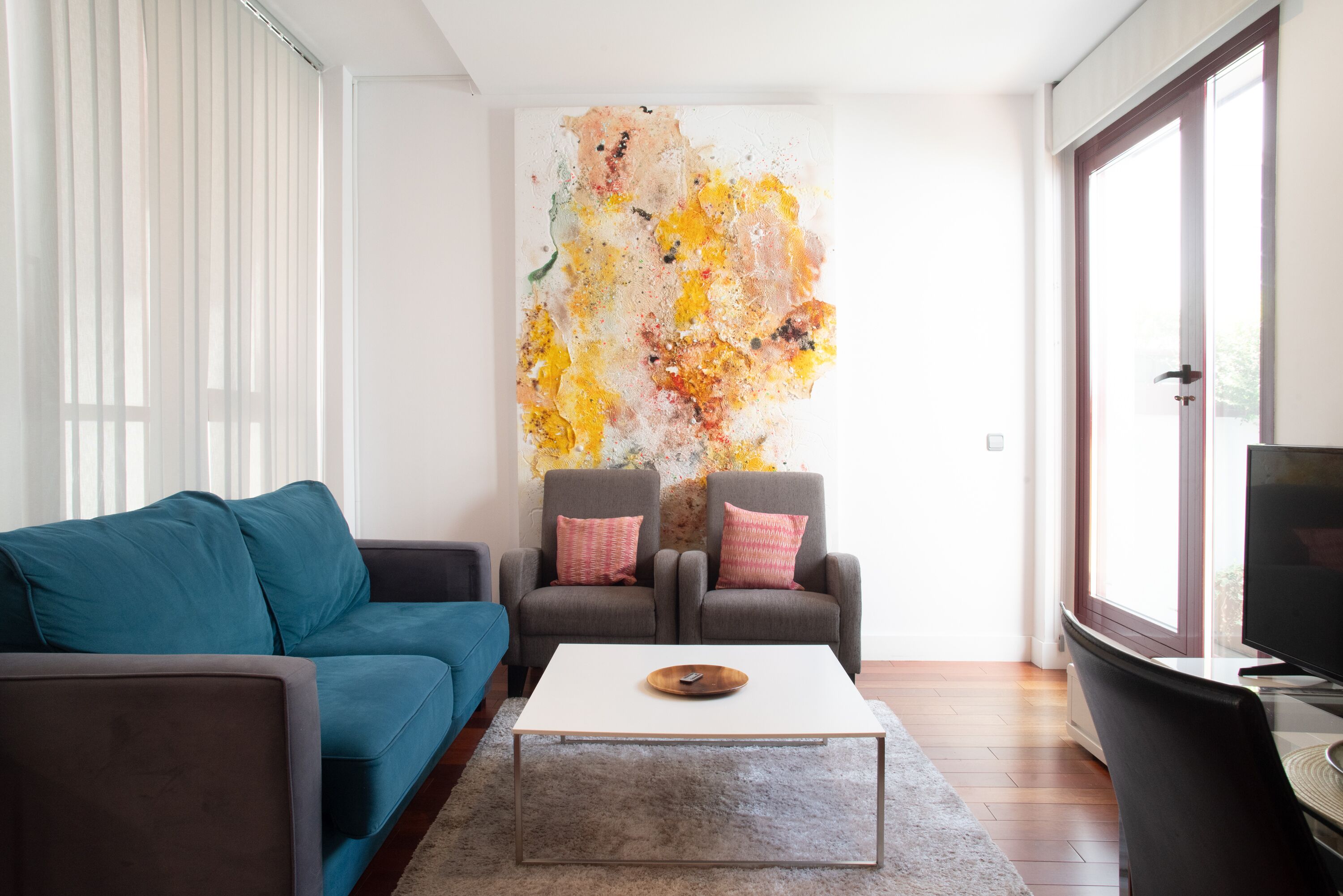 Un salon moderne avec un canapé de couleur turquoise, deux fauteuils, une table basse blanche et un grand tableau abstrait accroché au mur.