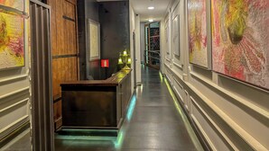 A hallway with a reception desk, framed artwork on the walls, and a staircase leading to another level. - Libertad 24 (Madrid)