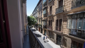 A narrow urban street with multi-story buildings, balconies, and a clear sky. - Libertad 24 (Madrid)
