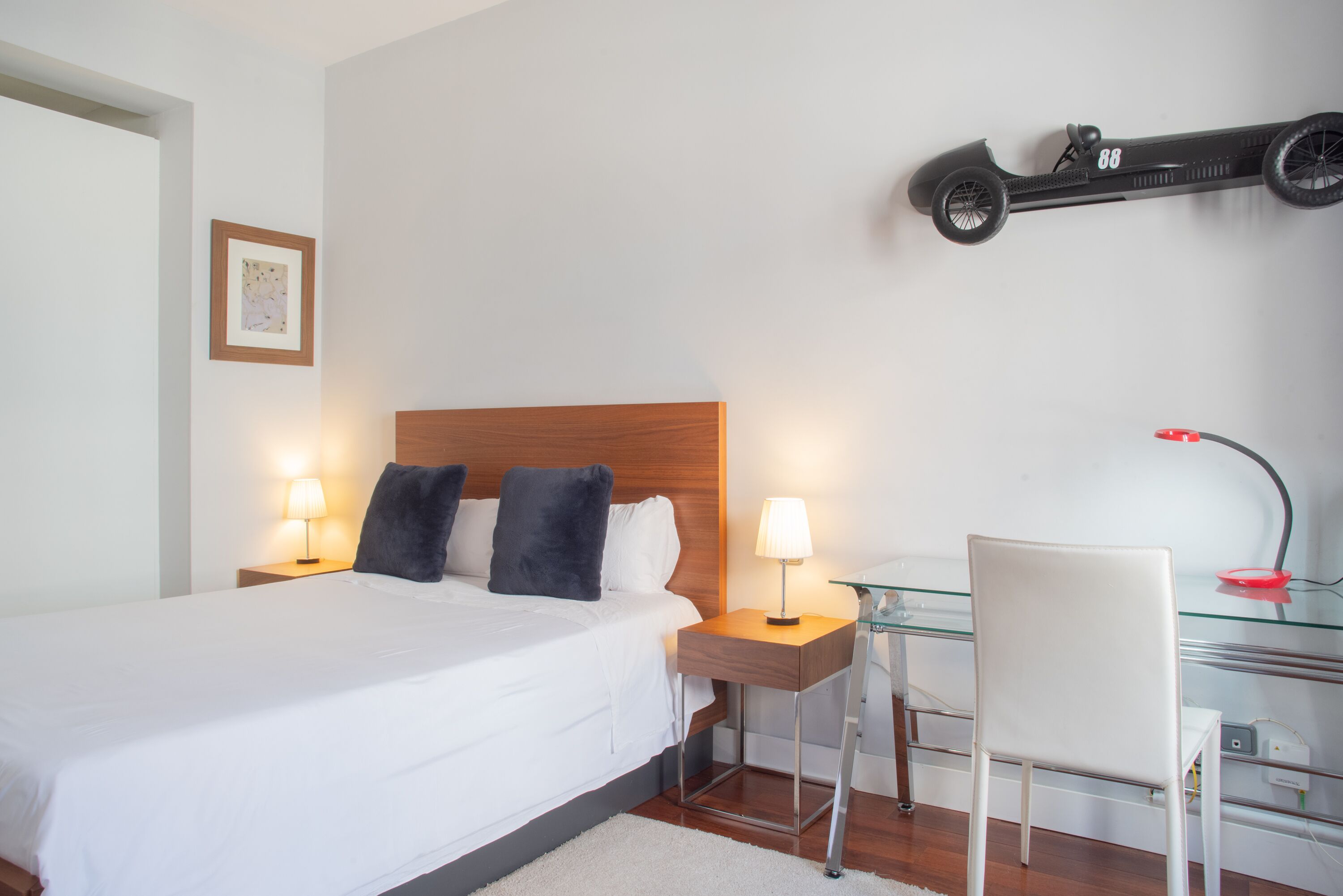 Habitación de hotel ordenada con cama, lámparas de noche, un escritorio con silla y una bicicleta fijada a la pared.