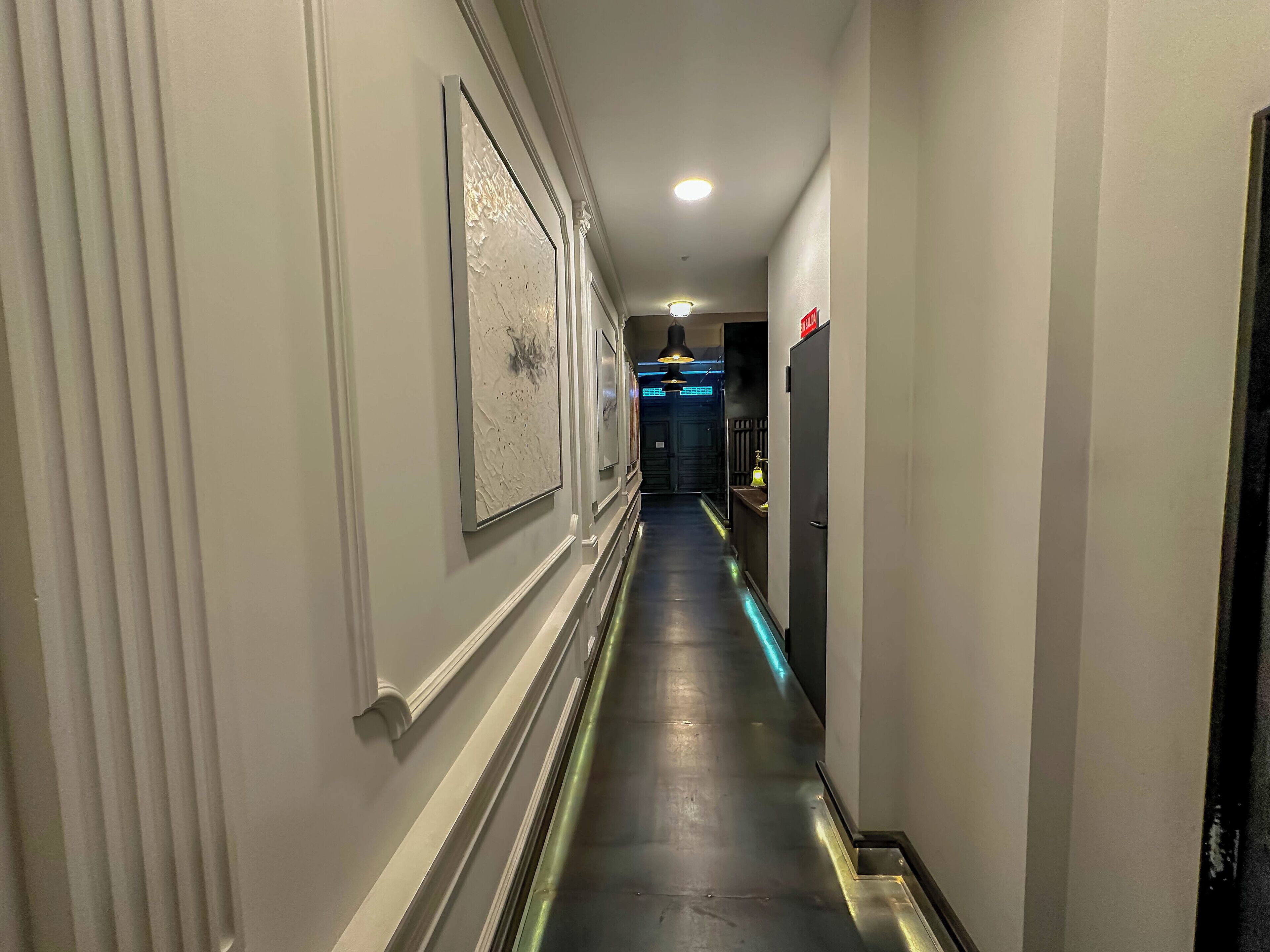Un pasillo de hotel largo, con obras de arte en la pared y una recepción al fondo.