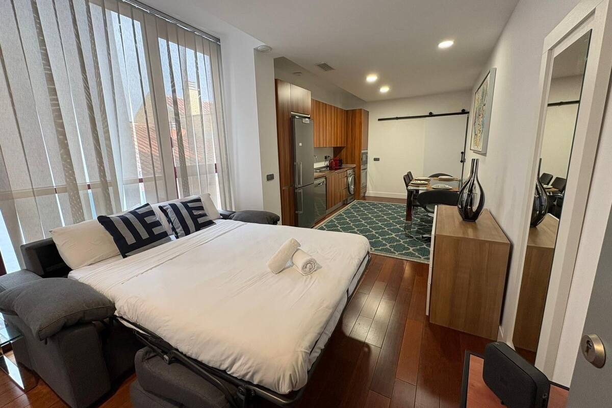 A modern hotel room with a bed, a desk, and a kitchenette.