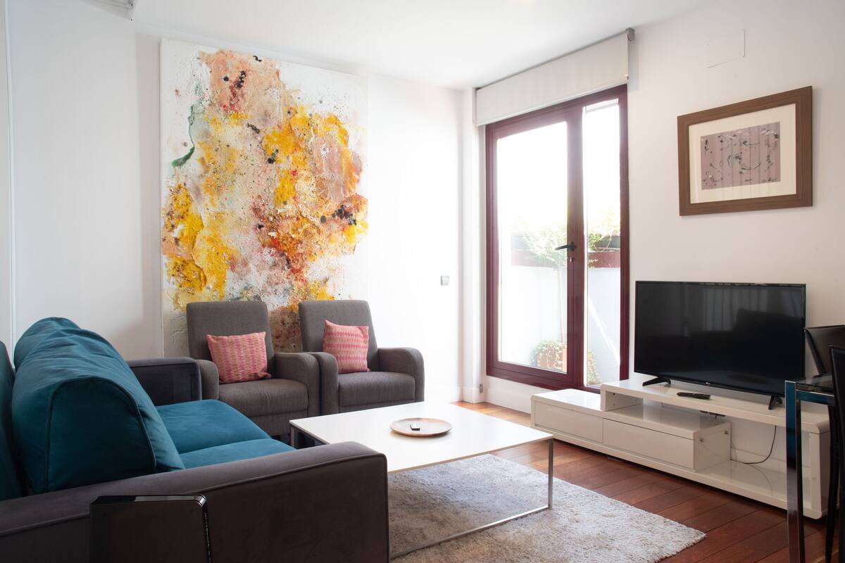 A modern living room with a large abstract painting, a flat-screen TV, and a sofa with teal cushions.