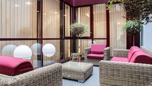 A modern indoor seating area with wicker furniture, a glass partition, and a potted plant. - Libertad 24 (Madrid)
