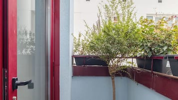 A small outdoor area with a red door, wooden flooring, and potted plants.