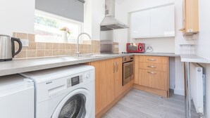 A modern kitchen with a washing machine, oven, and a window with a view. - Robins Perch (Stockport)