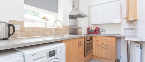 A modern kitchen with a washing machine, oven, and a window with a view.