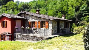 Une maison en pierre avec une façade rouge, des volets en bois et un balcon où se trouve un vélo.
