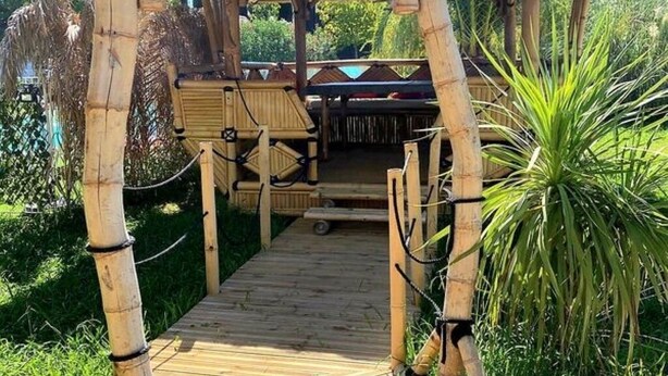 A wooden deck leading to a covered outdoor area with a seating arrangement. - Gîte Tropica Nîmes air-conditioned Swimming pool, slide, straw hut (Nîmes,Gard,)