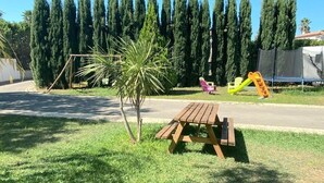 A picnic table in a grassy area with a playground in the background. - Gîte Tropica Nîmes air-conditioned Swimming pool, slide, straw hut (Nîmes,Gard,)