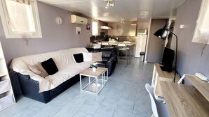 A modern living room with a sofa, a coffee table, and a dining area with a table and chairs. - Gîte Tropica Nîmes air-conditioned Swimming pool, slide, straw hut (Nîmes,Gard,)