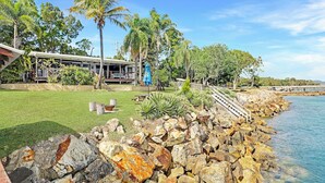 A coastal property with a stone wall, a grassy lawn, and a building with a porch.