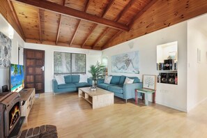 Un salon avec un plafond en bois, un ensemble de canapés, une table basse, une cheminée et une bibliothèque.