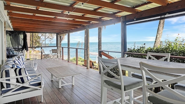 A covered outdoor seating area with wooden tables and chairs, overlooking a body of water.
