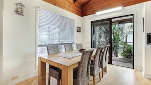 A dining area with a wooden table and wicker chairs, a window with blinds, and a sliding glass door leading to a garden.