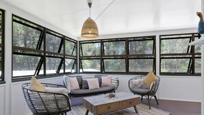 A sunroom with large windows, a wicker chair, a sofa, and a wooden coffee table.
