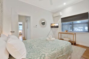 A bedroom with a bed, a bedside table with a basket, a TV, and a window with a view.