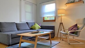 A living room with a grey sofa, a wooden coffee table, a striped rug, a floor lamp, and a white rocking chair.