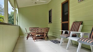 A room with a wooden bench and two striped chairs, a window with a 'Enjoy' sign, and a ceiling fan.