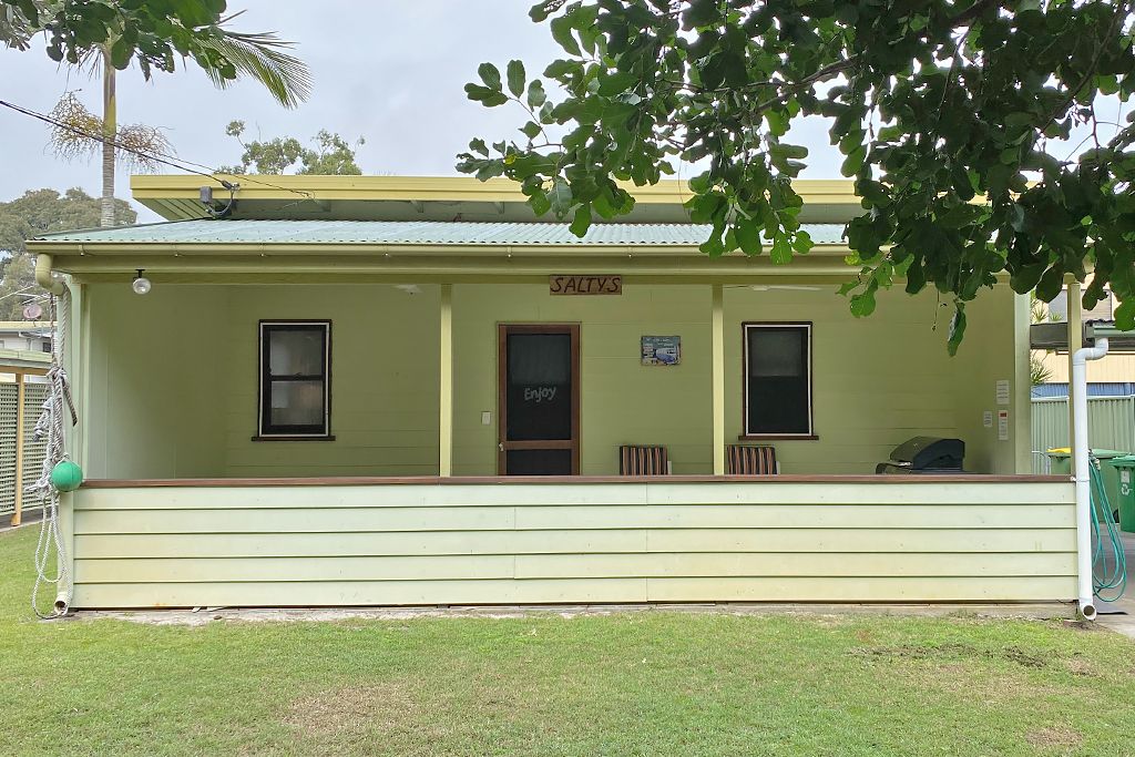 A single-story building with a green facade, a sign reading "SALTYS," and a small porch area.