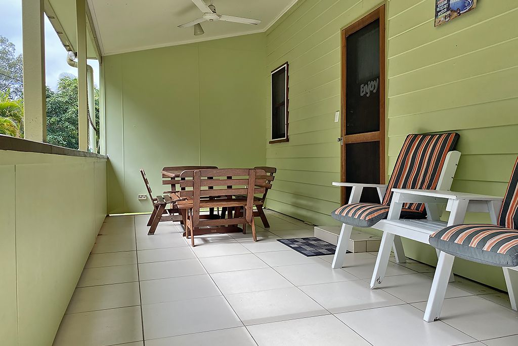 A room with a wooden bench and two striped chairs, a window with a 'Enjoy' sign, and a ceiling fan.