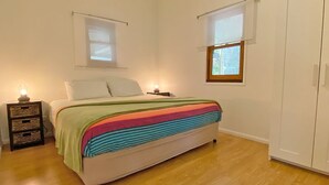 A bedroom with a bed, two bedside tables, a wardrobe, and two windows.