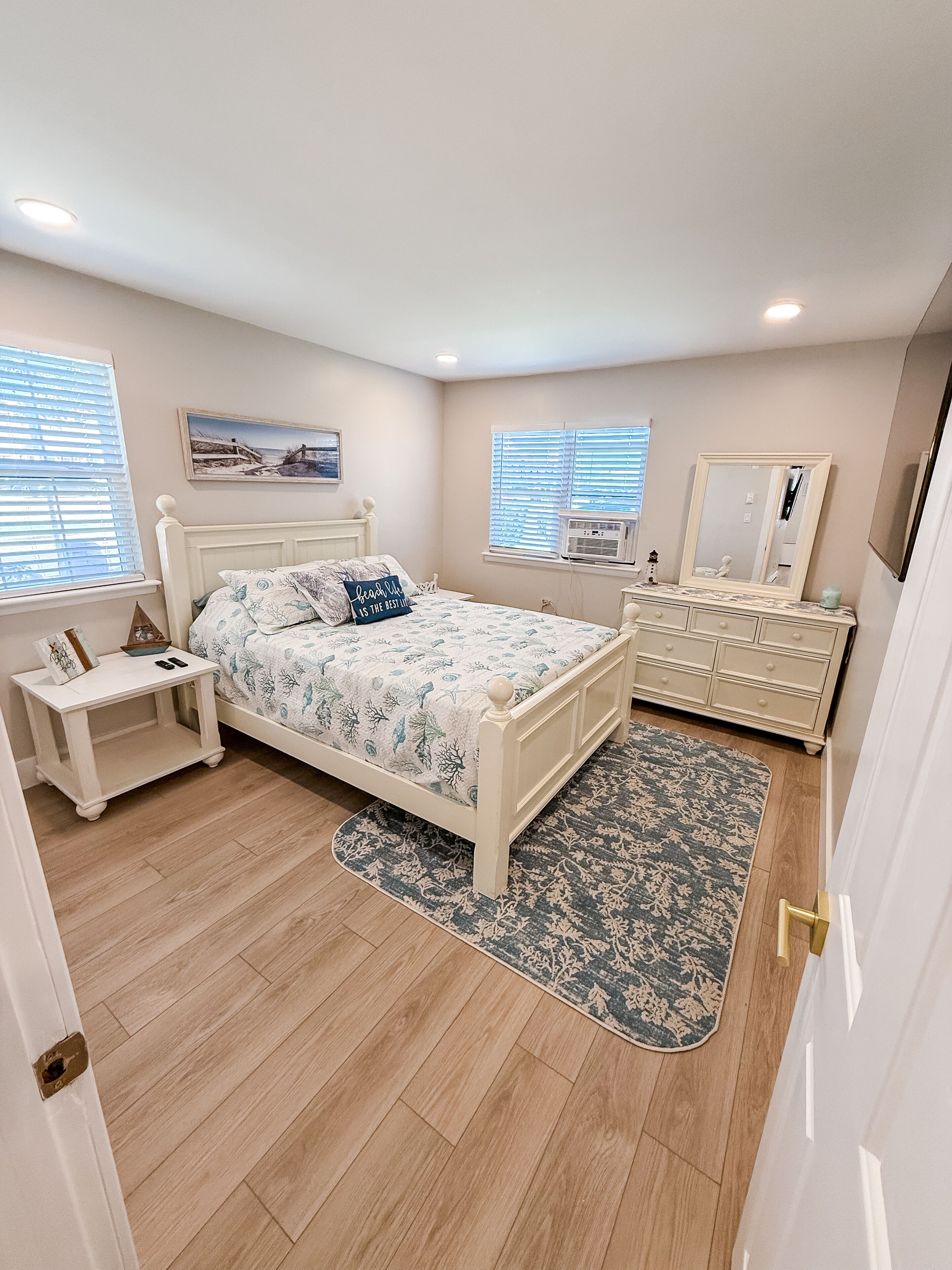 A bedroom with a bed, bedside table, dresser, and a large mirror.