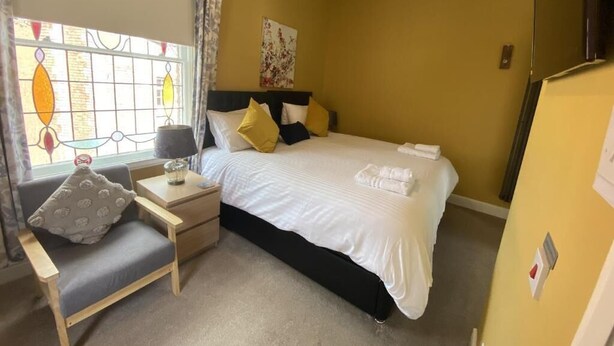 A hotel room with a bed, bedside table, lamp, and a window with curtains. - Grosvenor Place Guest House (Chester)