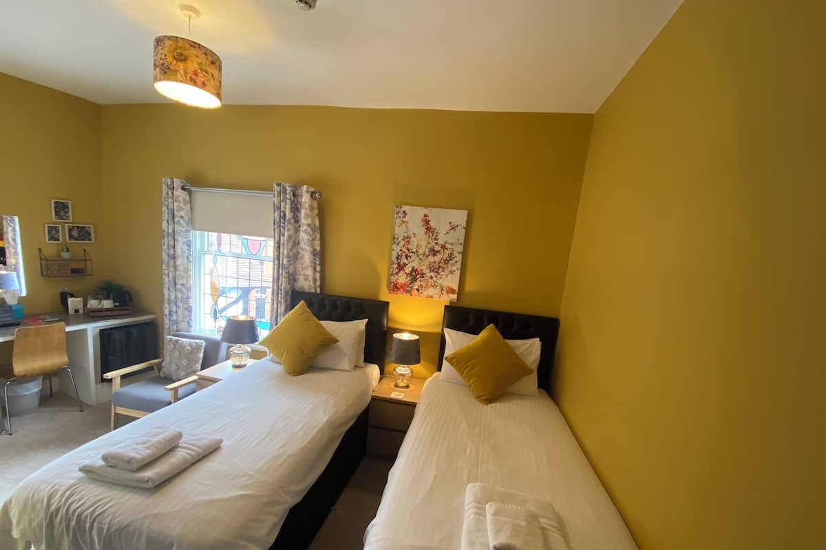 A hotel room with two beds, a desk, a chair, and a window with curtains.