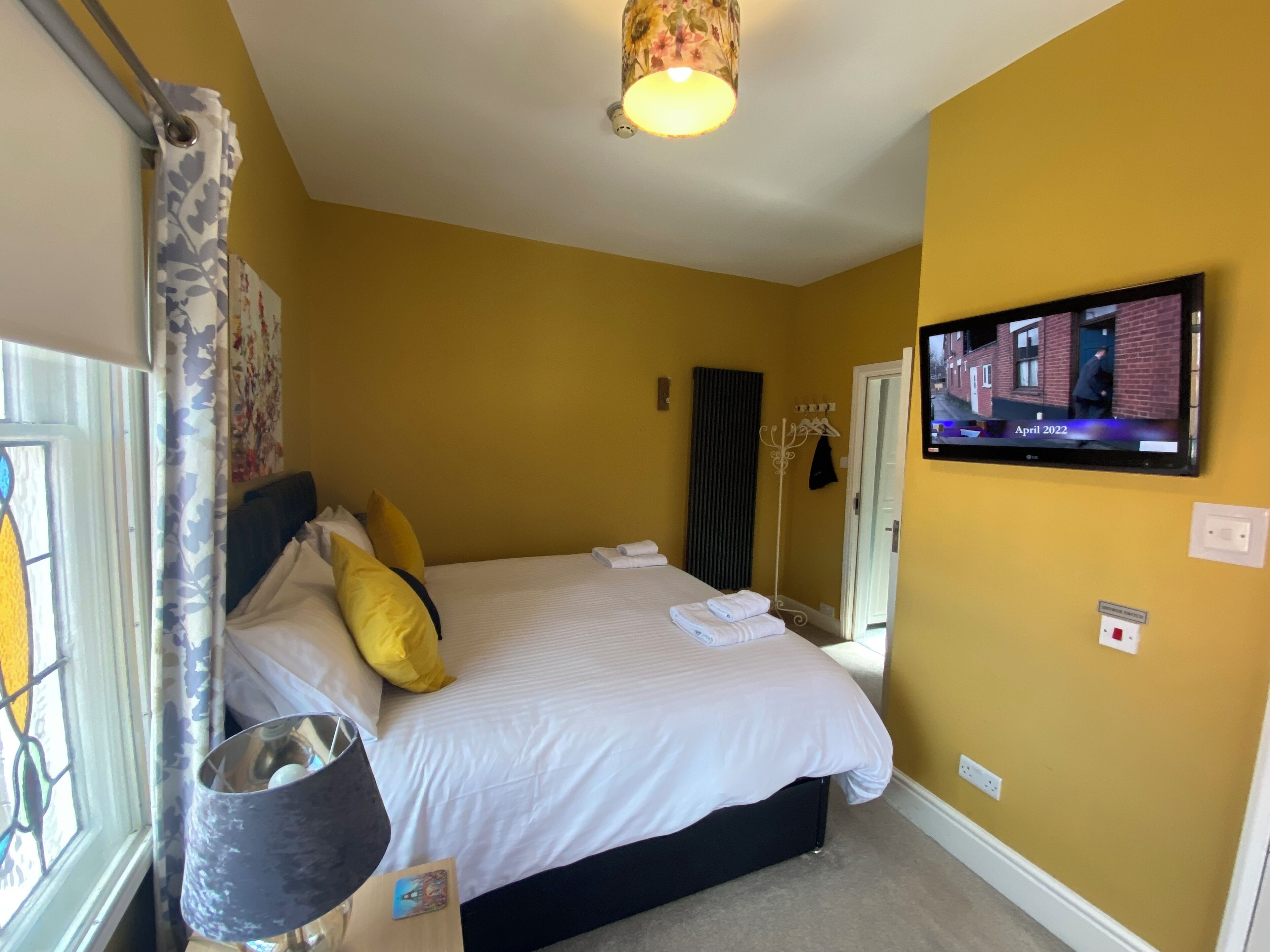 A bedroom with a bed, a television mounted on the wall, and a window with curtains.