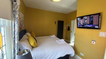 A bedroom with a bed, a television mounted on the wall, and a window with curtains.