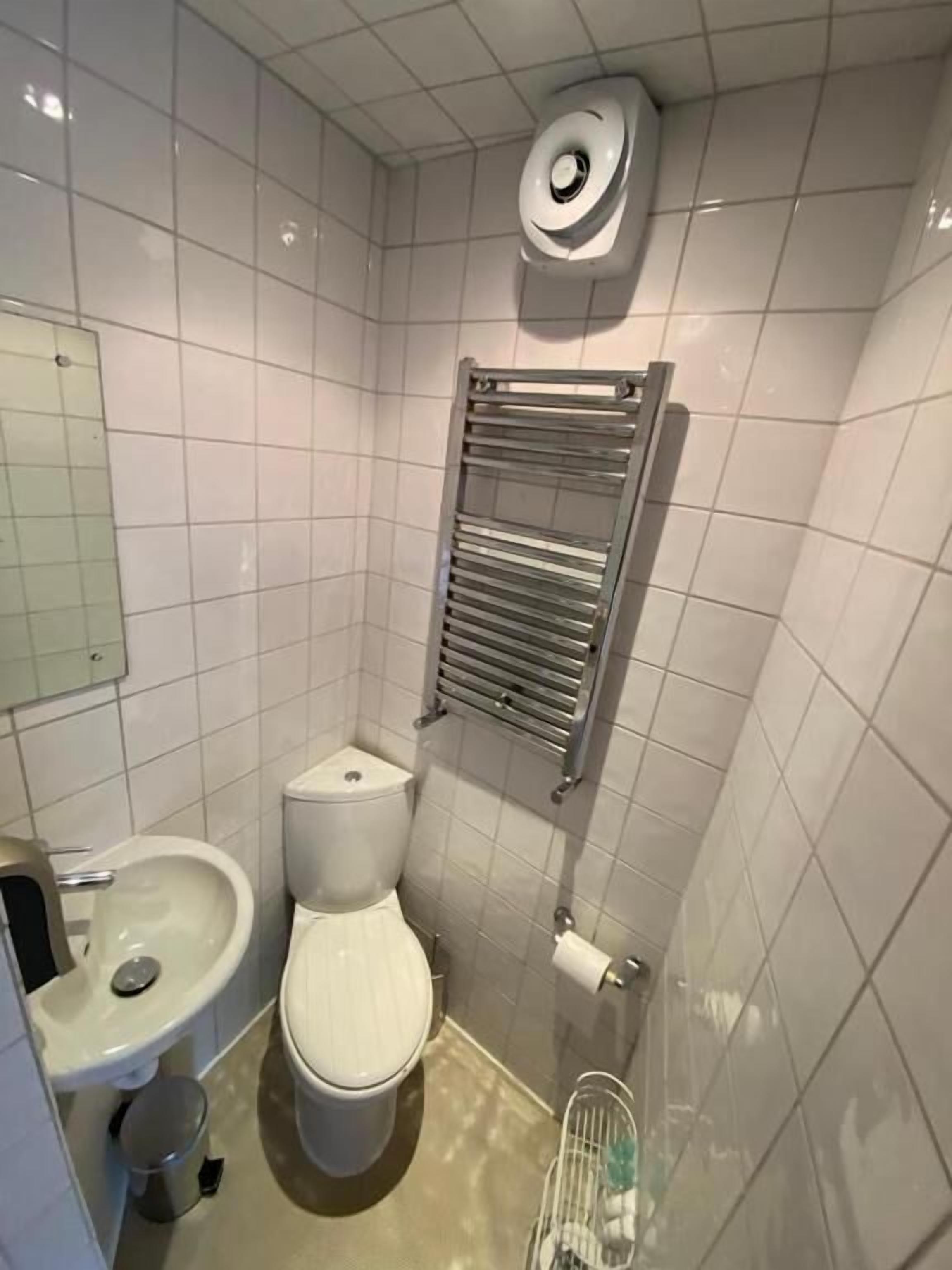 Ein kleines, modernes Badezimmer mit weißen Fliesen, einer Toilette, einem Waschbecken, einem Handtuchhalter und einem Toilettenpapierhalter.