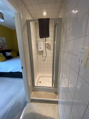 Une salle de bain moderne avec une douche à parois de verre, des murs recouverts de carreaux blancs et une prise électrique visible.