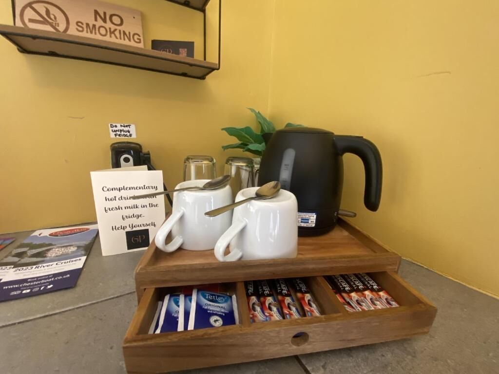 Una estación de café con tazas, una tetera y una bandeja de bolsitas de té.