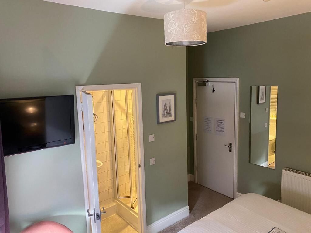 A bedroom with a bed, a TV mounted on the wall, a door leading to a bathroom, and a mirror on the wall.