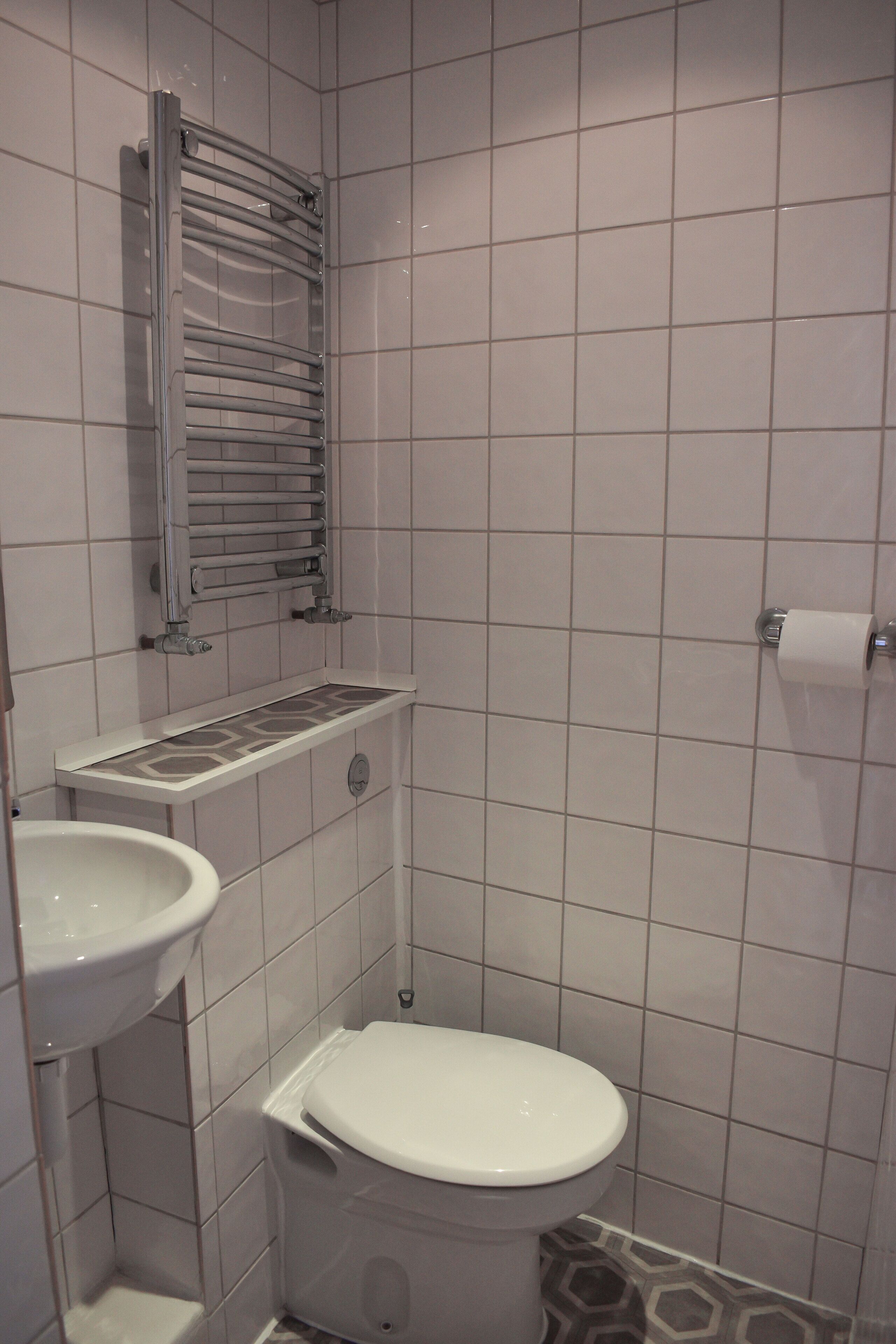 Um banheiro pequeno revestido com azulejos, com vaso sanitário, pia e porta-toalhas.
