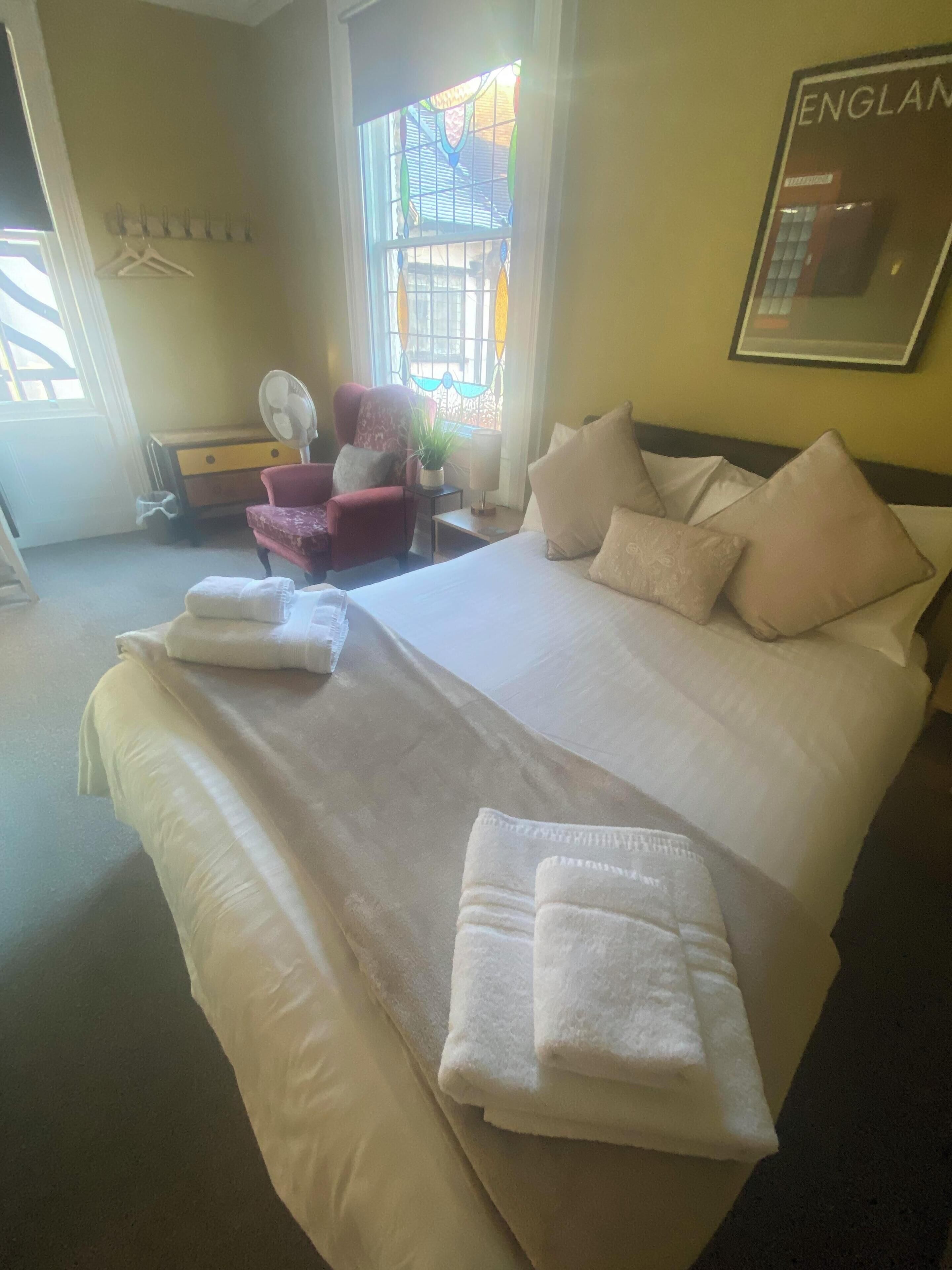 A hotel room with a large bed, a chair, a small table with a lamp, and a window with a view of the outside.