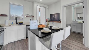 Une cuisine moderne avec des meubles blancs, un plan de travail noir et un coin repas avec des chaises blanches.