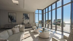 A spacious room with a large window overlooking a beach, a modern sofa, and a minimalist decor. - The Oasis at Orange Beach 1002 (Orange Beach)