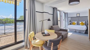 Habitación de hotel moderna con un balcón grande, una mesa de comedor redonda, un sofá y una cama con vistas a la ciudad.