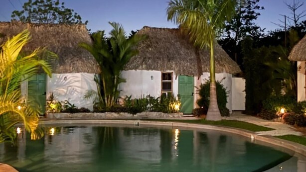 A pool area with thatched-roof structures, palm trees, and a clear night sky. - Hotel Kocai Izamal  (Izamal)