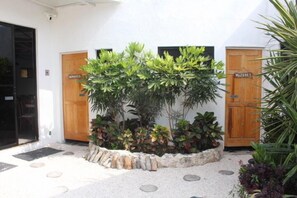 A courtyard with a stone pathway, two wooden doors labeled 'HIMBRES' and 'MUJERES,' and a variety of potted plants. - Hotel Kocai Izamal  (Izamal)