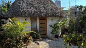 A thatched-roof house with a wooden door, surrounded by gravel and plants. - Hotel Kocai Izamal  (Izamal)