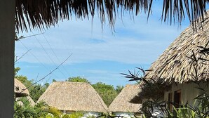A view of thatched-roof huts with a pool and tropical plants in the foreground. - Hotel Kocai Izamal  (Izamal)