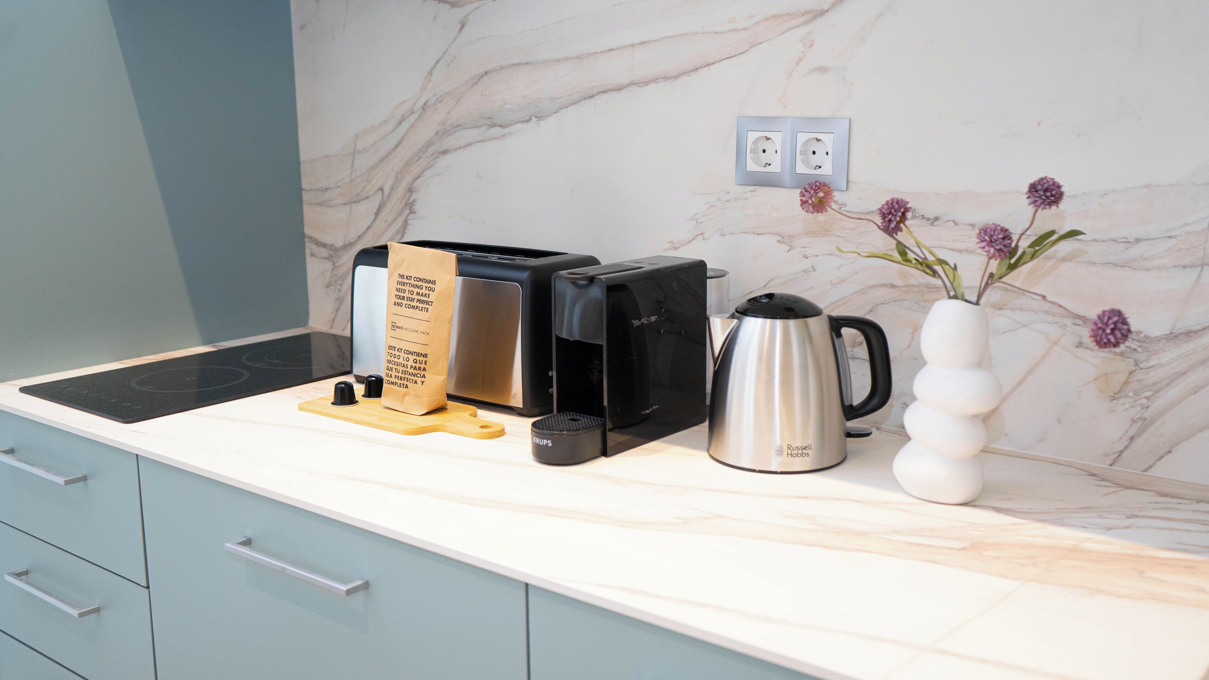A kitchen with a toaster, kettle, and a vase with flowers on the counter.