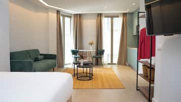 Een moderne hotelkamer met een groene bank, een ronde tafel met een bloevas, en een televisie op een dressoir.