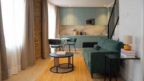 Un salon moderne avec un canapé vert, une petite table ronde et un coin cuisine à l’arrière-plan.