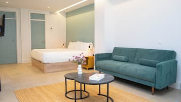 Een slaapkamer met een bed, een groene bank, een kleine tafel met een boek en een vaas met bloemen.