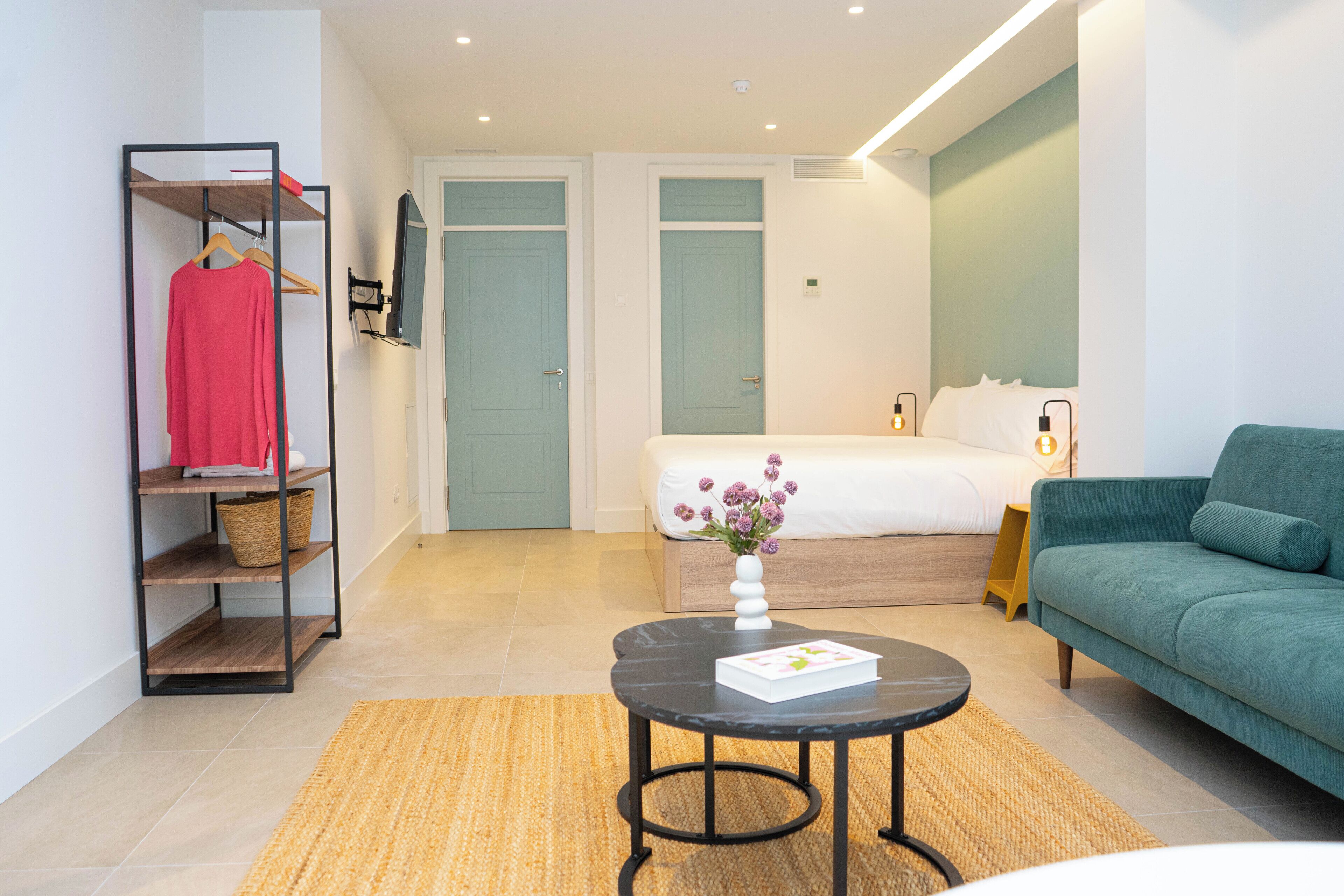 Una habitació d'hotel moderna amb un llit, un sofà verd, una taula rodona petita i una estant per a roba.